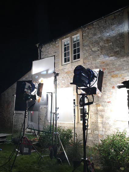 Three lighting fixtures positioned outside a stone building, illuminating the area during nighttime.
