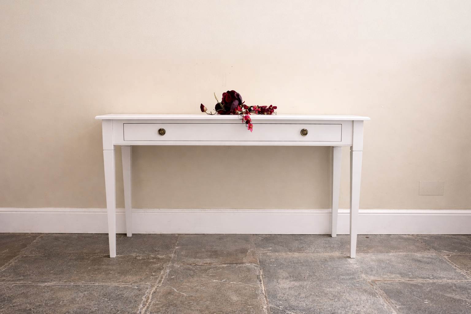 White console table with a single drawer, adorned with a decorative arrangement of dried flowers.