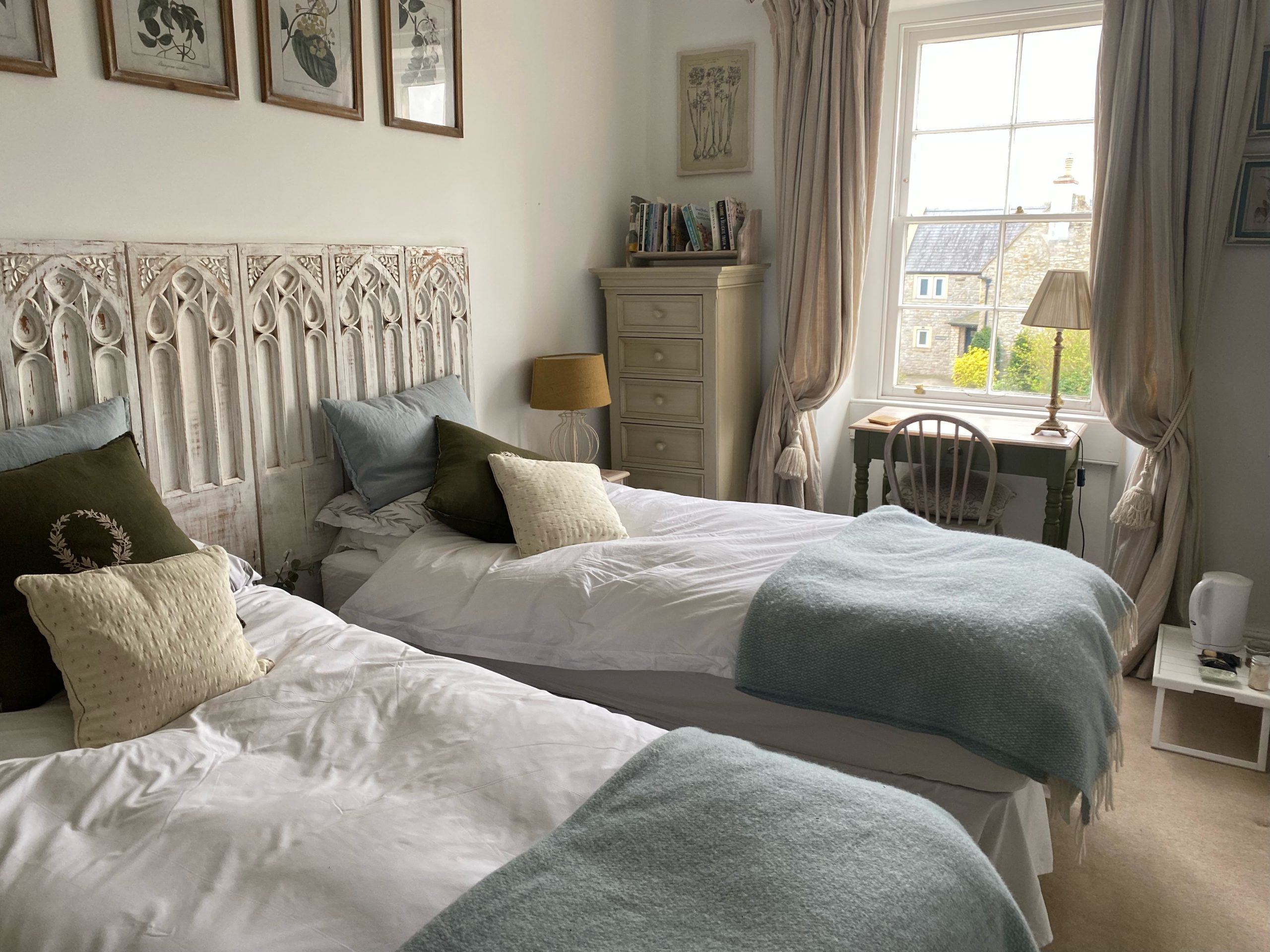 Twin beds with decorative headboard, soft cushions, and a light blue throw in a well-lit room.